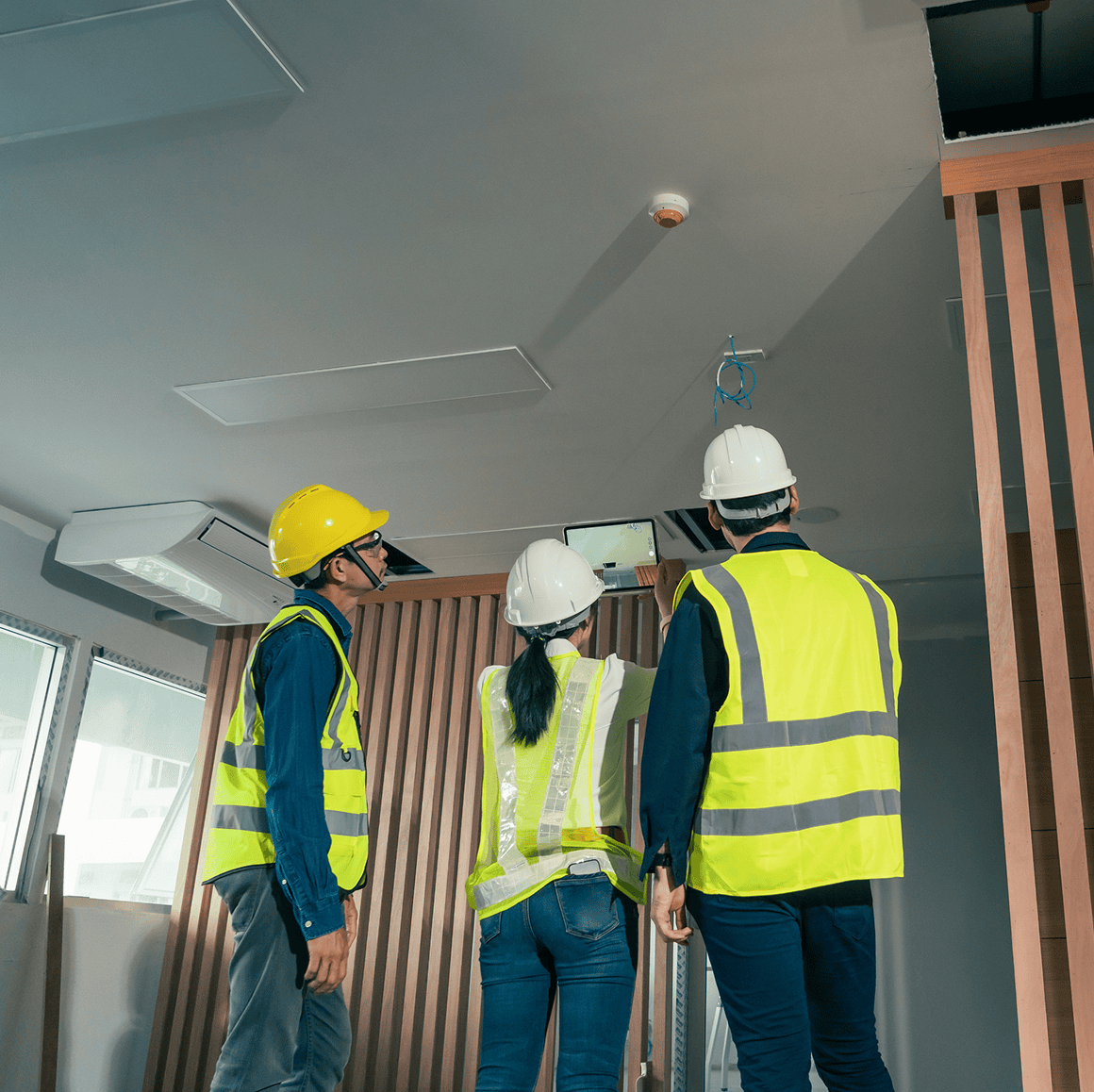 Construction workers inspecting ceiling installation indoors.